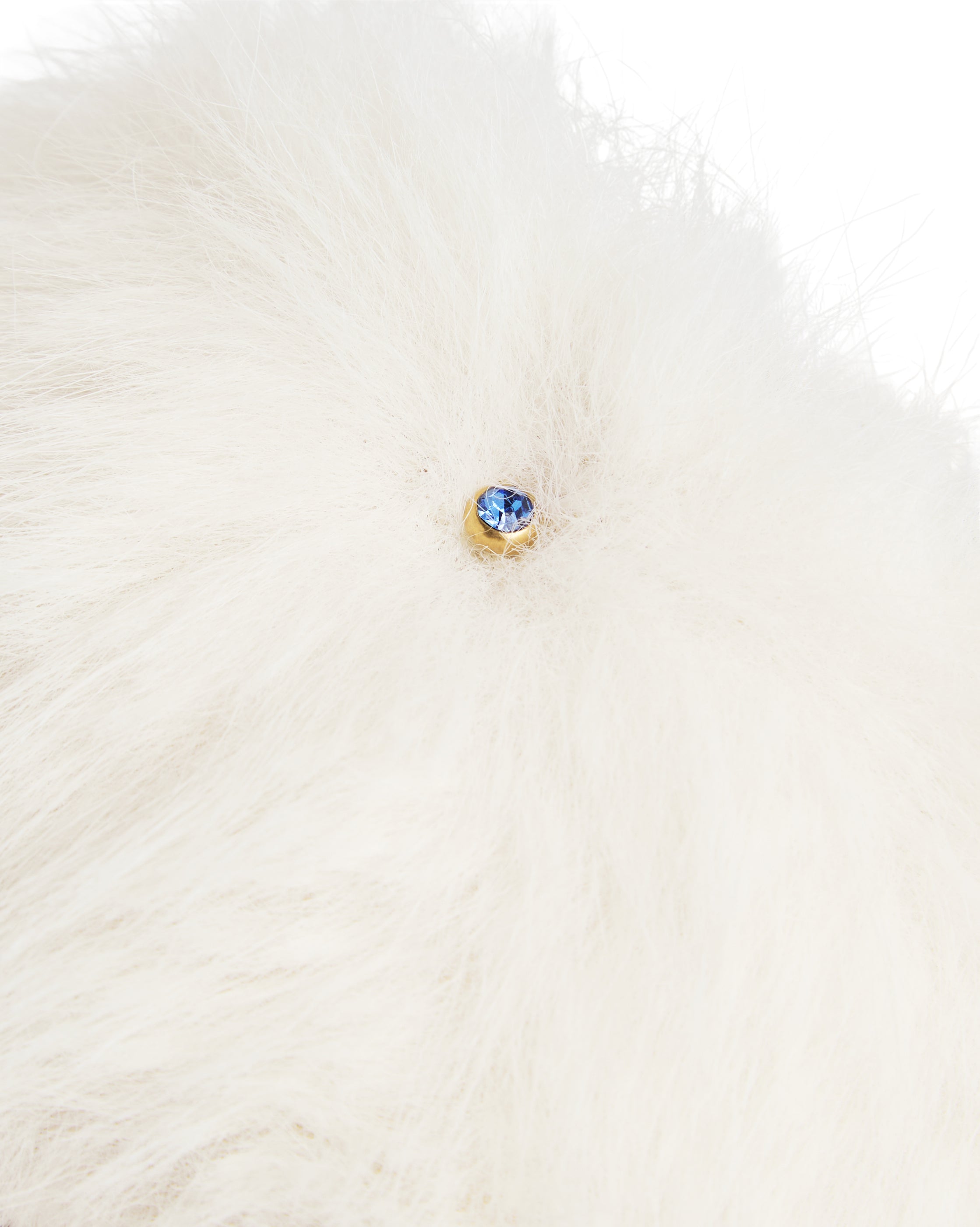 Detalhe do pingente em cristal azul na faixa de pelo creme do chinelinho da linha Serenitá Benvenuta.